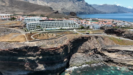 fantastic aerial shot in orbit over the hotels and buildings on the coast of the port of agaete on a sunny day and the island of gran canaria