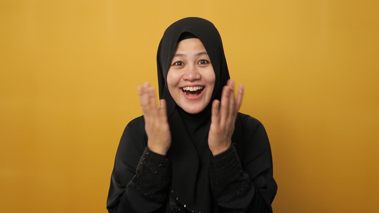 히자브를 입은 귀여운 젊은 아시아 무슬림 여성의 초상화는 노란색에 대비하여 큰 눈과 열린 입으로 놀랐거나 충격을 받은 표정을 보여줍니다.