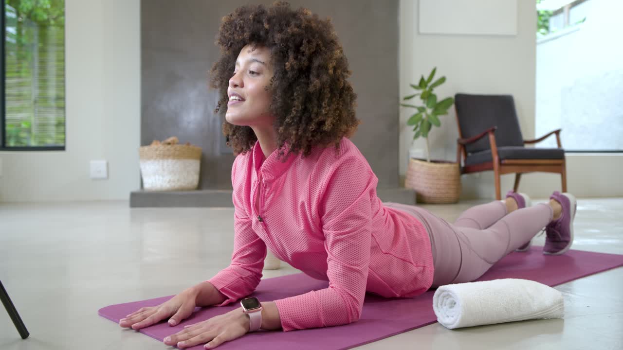 Tripod filming African American woman shifting from plank to cobra stretch on yoga mat for fitness
