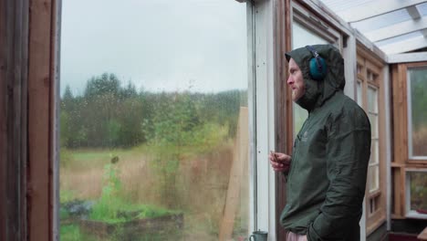 a man in a hooded jacket looking at the glass window while eating crackers