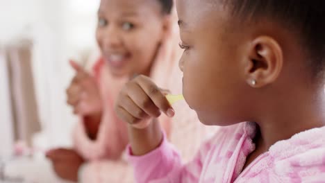 Happy-unaltered-african-american-mother-and-daughter-brushing-teeth-in-bathroom,-in-slow-motion