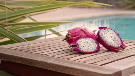 sliced dragon fruit on wooden table with swimming pool in the background at sunset lateral shot