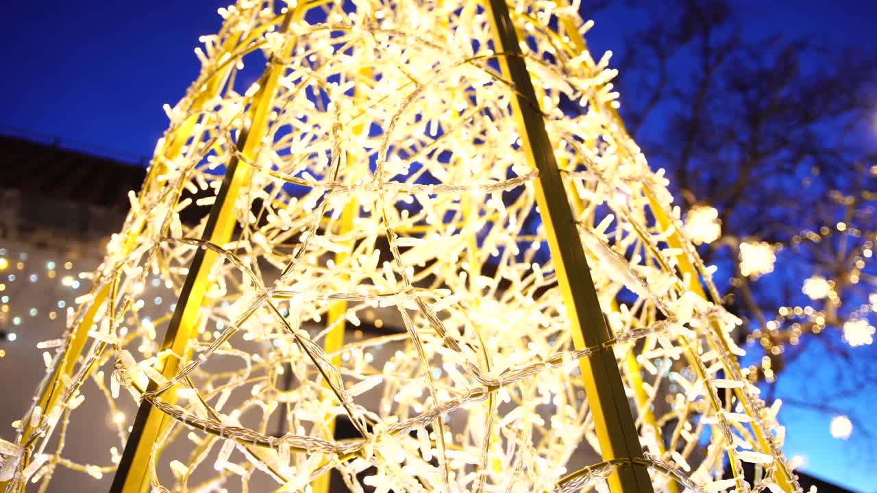 Cone-shaped Christmas tree made of garlands, against the background of the black sky.