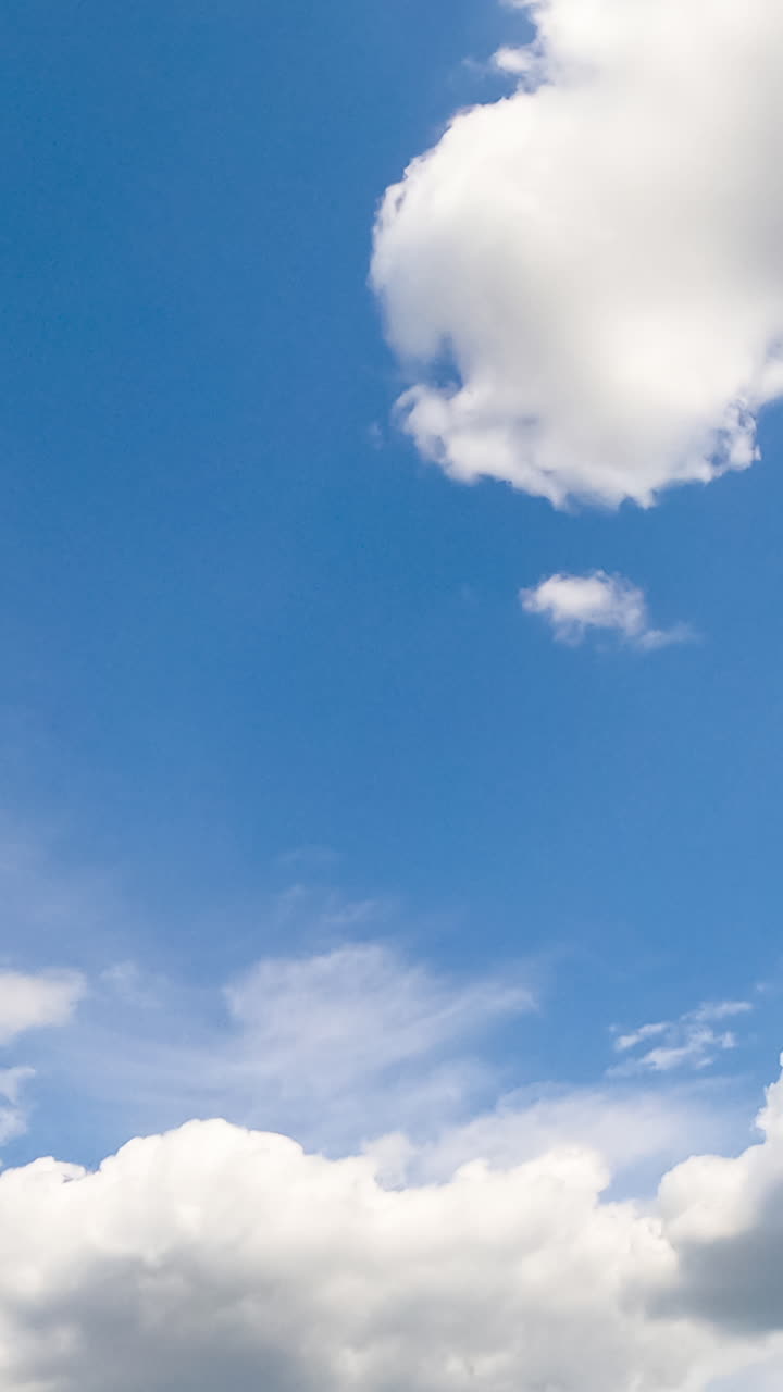 Light blue summer sky with fluffy soft clouds. White cloudscape formation from low angle view. Vertical video
