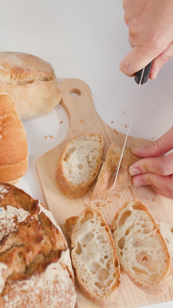 Close-up of hands cutting artisan bread on a wooden board against a white background.