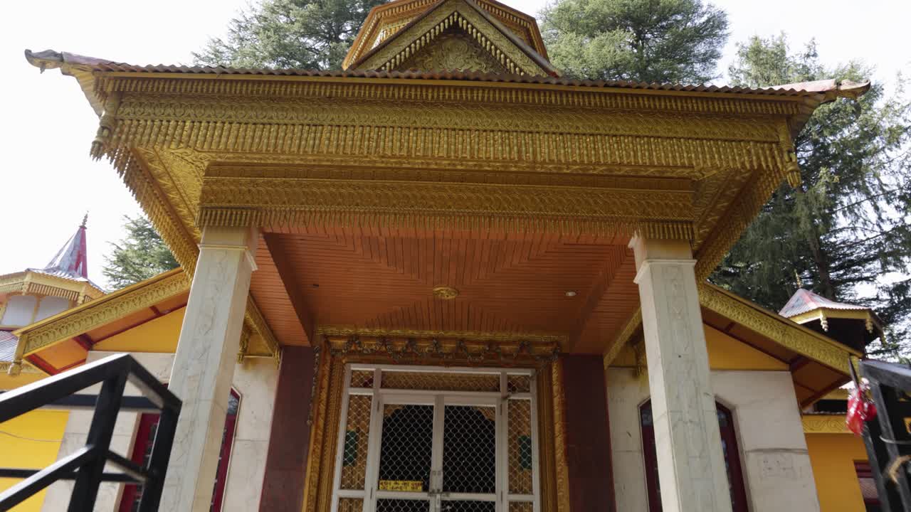 Pintu masuk kuil Hindu berukir dengan atap emas dan detail ukiran di tengah hutan, gambar diambil di Kuil Jai Maa Tara Devi Shimla.