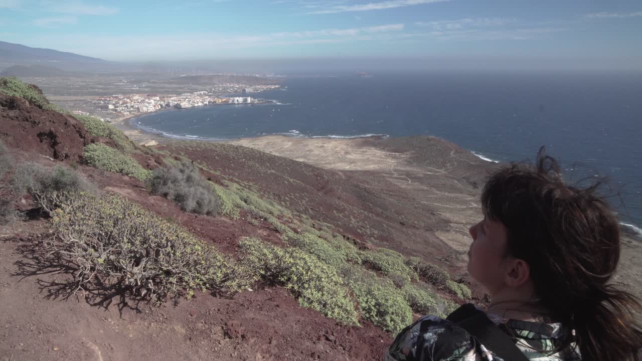 chica de pelo largo mira hacia abajo desde la montaña hasta las playas de la isla de tenerife