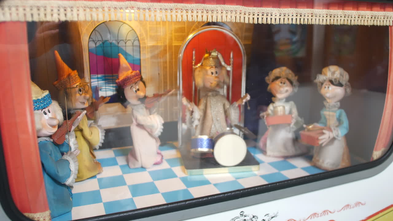 A puppet show set in a themed display box is depicting characters in colorful outfits performing with instruments and props framed by curtains and theatrical decor