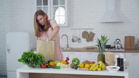 happy housewife with fresh fruit and vegetables in the kitchen. young woman unpack organic food from paper bag at home.