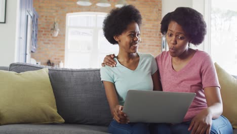 Happy-african-american-mother-and-daughter-sitting-on-sofa-using-laptop