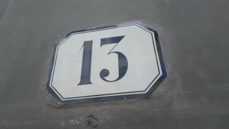 Arcing-shot-of-number-13-door-sign-in-shade,-during-day-time