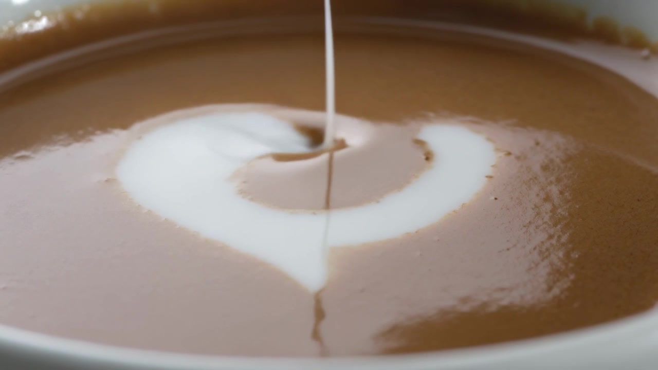 Goccia che si posa sulla crema, tazza di caffè che riceve un getto di latte al bar, formando una latte art a forma di cuore.