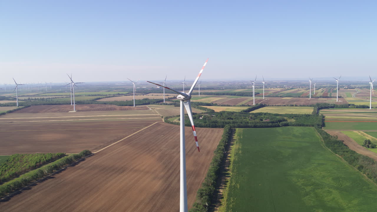 Grand vista aerial of renewable energy wind farm turbines amongst farm land and crop fields