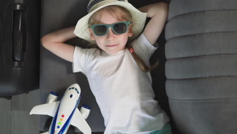 preschooler girl in sunglasses looks in camera lying on sofa