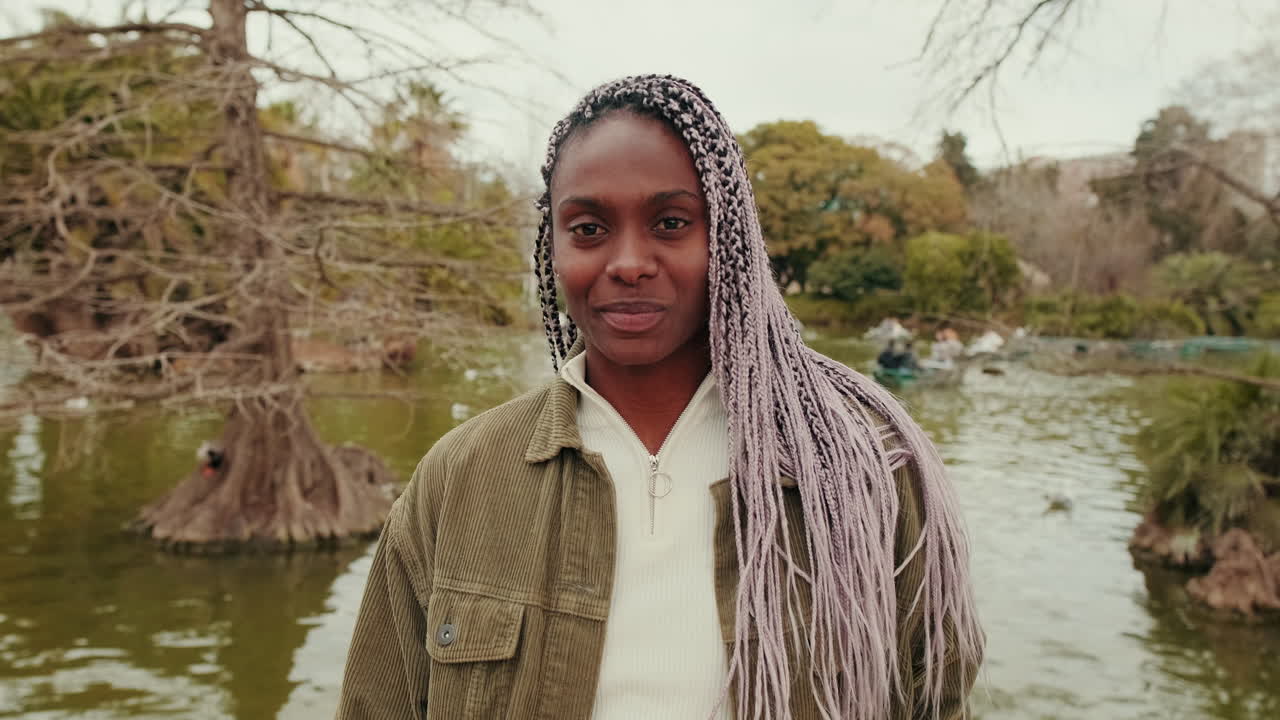Young African American Woman with Braids Smiling by a Lake in a Park