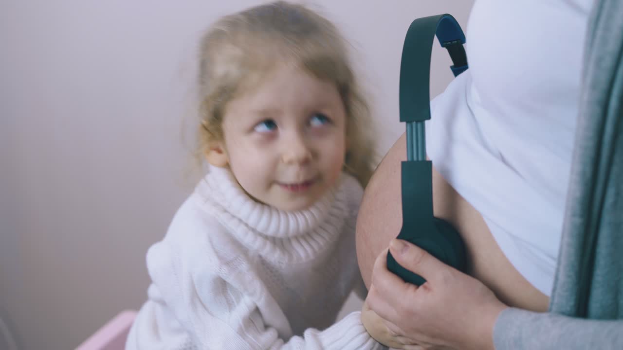 милая девушка слушает ребенка в животе матери с наушниками