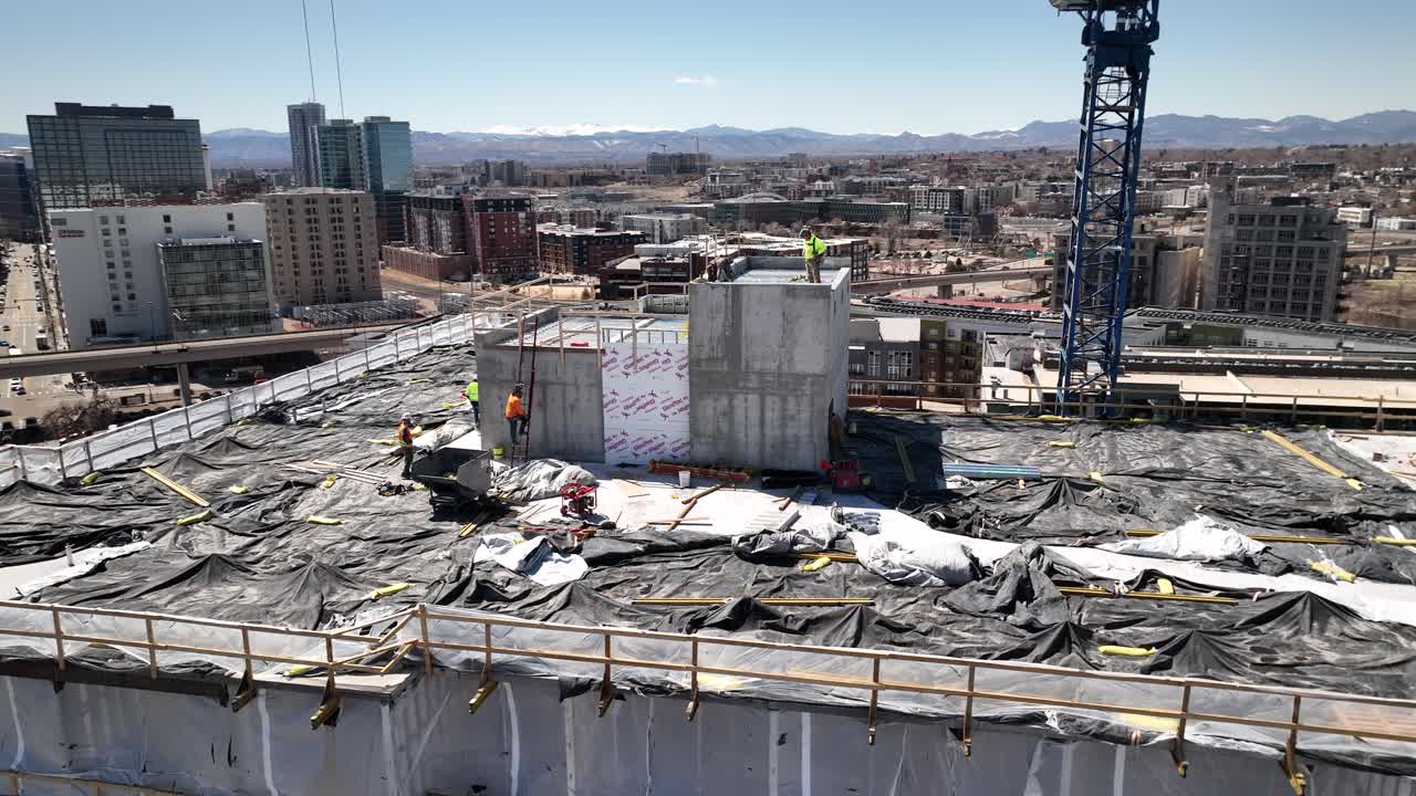 Construction workers move around rooftop of new building development, aerial