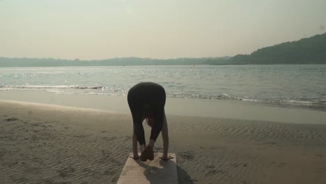 view of girl doing vinyasa yoga along the beach with tide lapping the shoreline in background