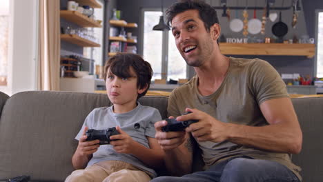 father and son sitting on sofa in lounge playing video game