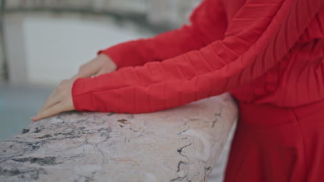 closeup woman hands resting concrete border at square. red dress lady relaxing