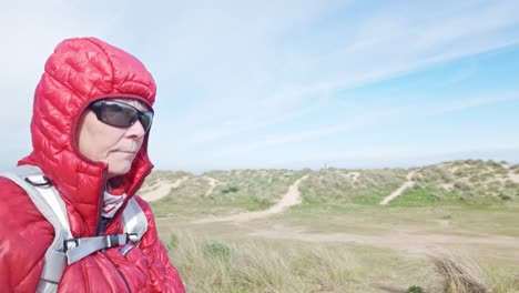 Woman-hikes-along-Suffolk-coastal-path-sand-dunes-wearing-wind-cheater