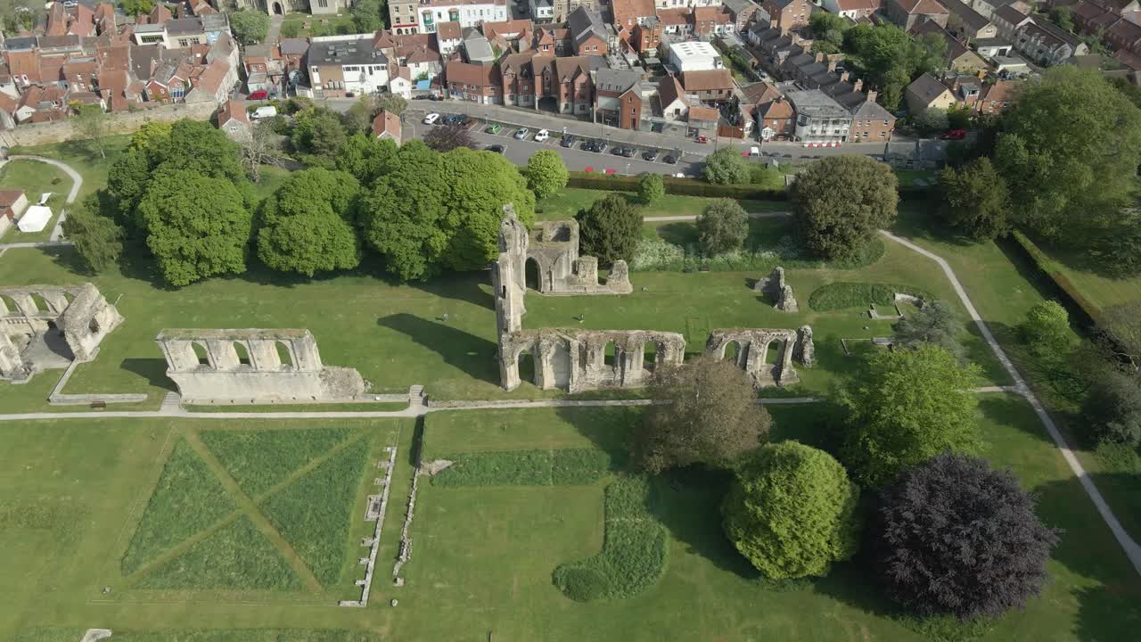Aerial view of the Glastonbury Abbey ruins an 8th century monastery and gardens. Drone moving to the left showing the abbey ruins and the trees that surrounds it. 4K, 60fps.
