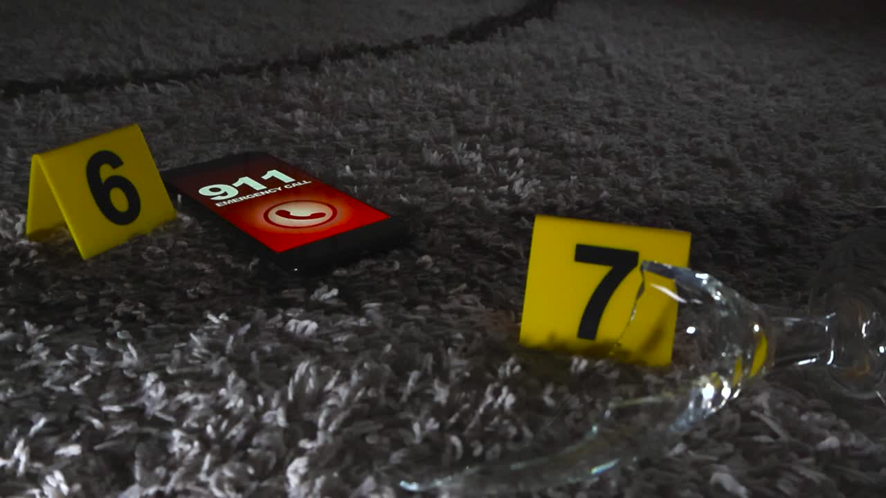 Closeup low angle gliding around forensic evidence markers placed beside shattered glass and cell phone emergency calling 911 lying on carpeted floor in a dark dimly lit room. Domestic crime scene