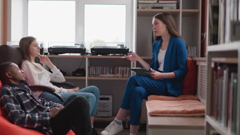 three young people sitting in a library, talking and working.