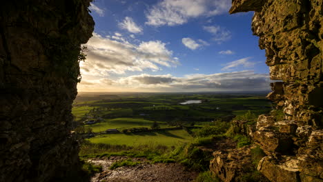 lapso de tiempo del paisaje agrícola rural con un lago distante en campos de hierba y colinas durante la puesta de sol nublada vista desde las cuevas de keash en el condado de sligo en irlanda