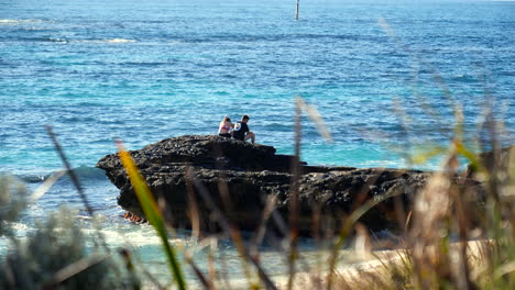 amantes sentados en rocas junto al océano