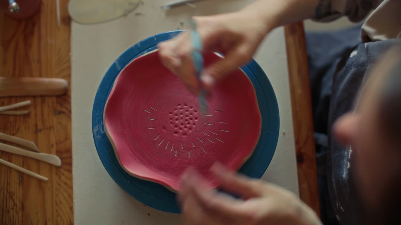 Top Down of Potter Drawing Pattern on Red Ceramic Bowl with Scribe Tool