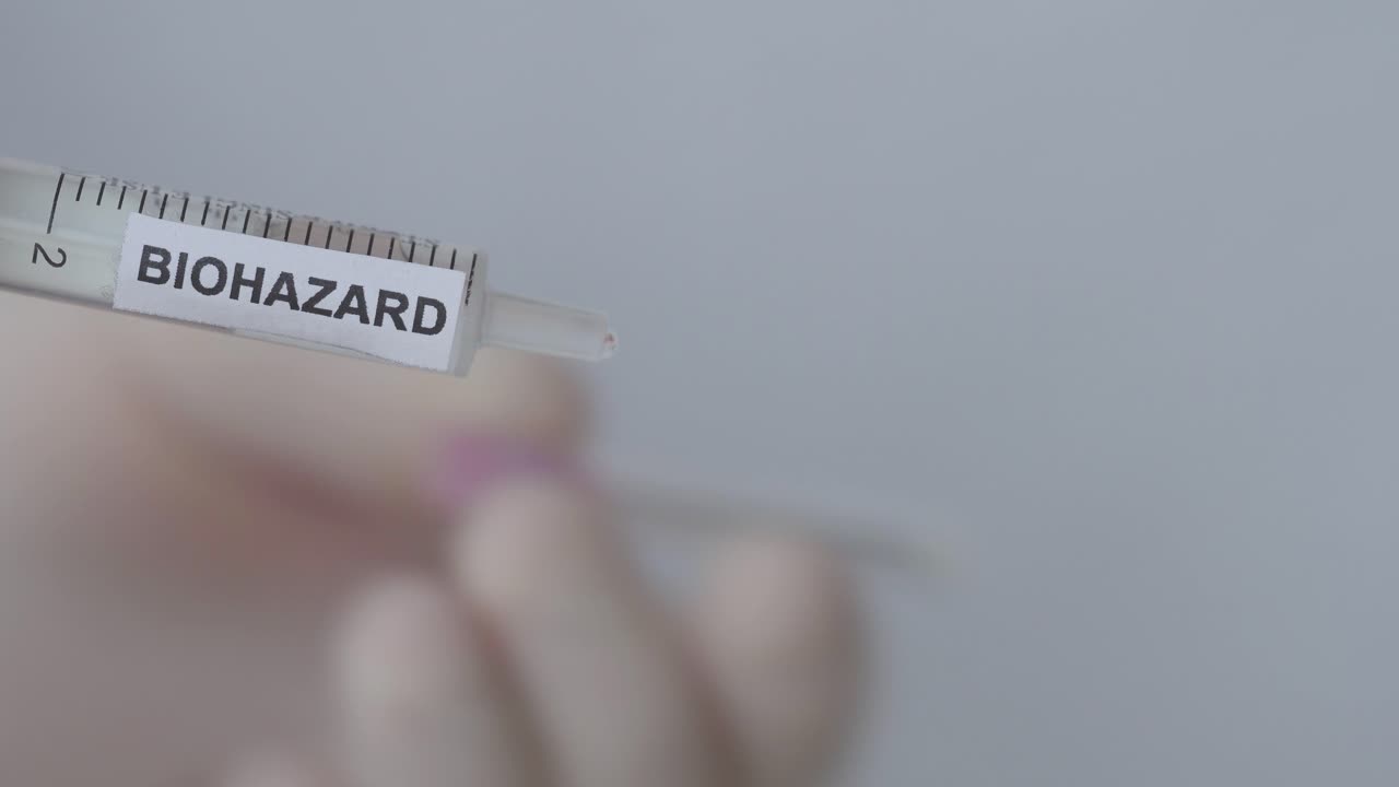 Attaching Hypodermic Needle To Syringe With Biohazard Label - Vaccination Concept - close up