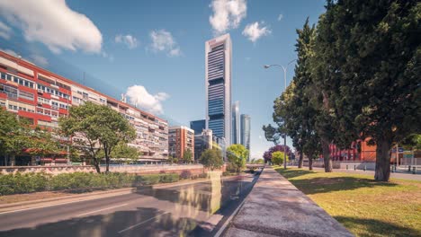 ultra ancho de derecha a izquierda pan timelapse de los rascacielos de madrid contra el cielo azul con nubes blancas en una soleada mañana de primavera de negocios y primer plano de automóviles que pasan