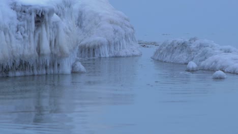 Pequeñas-Olas-Rompiendo-Contra-Las-Ruinas-De-La-Fortificación-De-Los-Fuertes-Del-Norte-De-Karosta-En-La-Orilla-Del-Mar-Báltico-En-Un-Día-Nublado-De-Invierno,-Cubierto-De-Hielo,-Nieve-Y-Carámbanos,-Toma-De-Primer-Plano-Medio