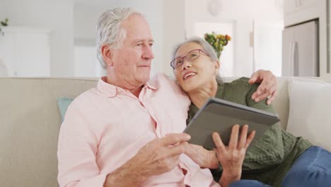 happy diverse senior couple using tablet and sitting on couch