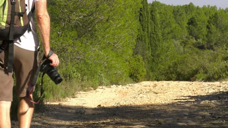 Man-with-camera-walking-on-hiking-trail,-slow-motion-low-angle