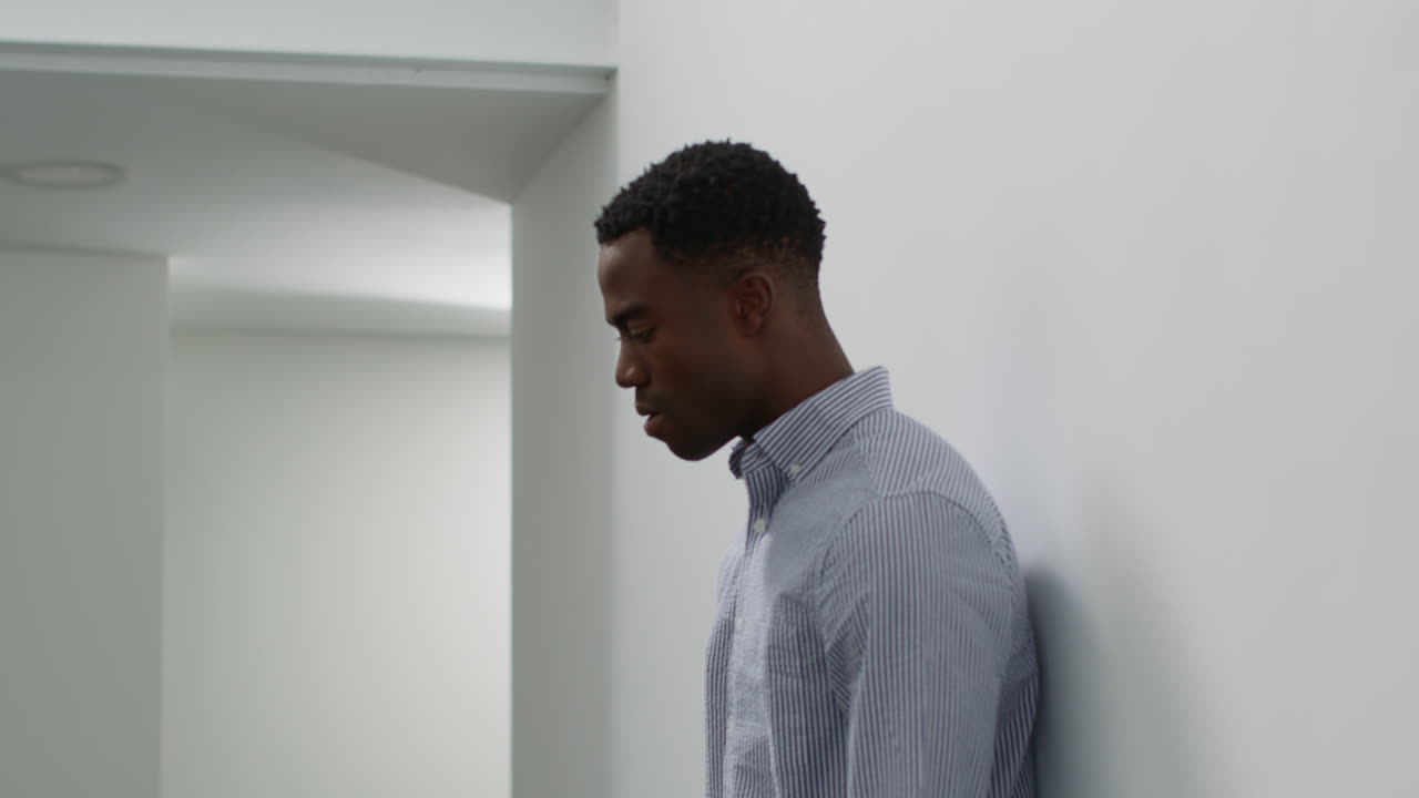 Young Businessman In Office With Mental Health Issues Leaning Against Wall Looking Unhappy And Depressed