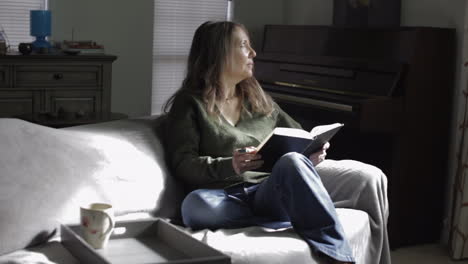 Beautiful-Adult-Caucasian-Woman-Pondering-Thoughts-While-Sitting-And-Holding-Book-At-The-Living-Room