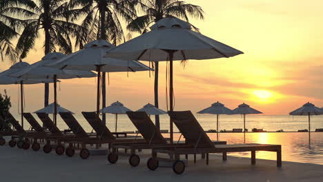 A-colorful-sunset-highlights-a-line-of-empty-sun-loungers-and-beach-umbrellas-along-the-edge-of-a-resort-swimming-pool