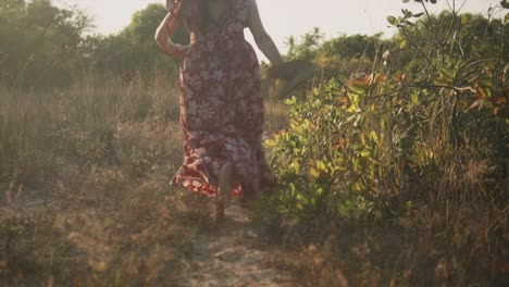 Una-Mujer-Caucásica-Emocionada-Con-Un-Vestido-Floral-Rojo,-Corriendo-Descalza-Hacia-La-Puesta-De-Sol-Dorada-En-Un-Hermoso-Día-Al-Aire-Libre