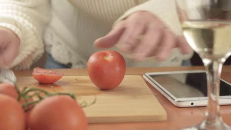 hands cutting fresh vine tomatoes in kitchen with recipe on tablet medium shot