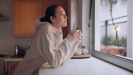 mujer, taza de café y pensando por la ventana de la cocina