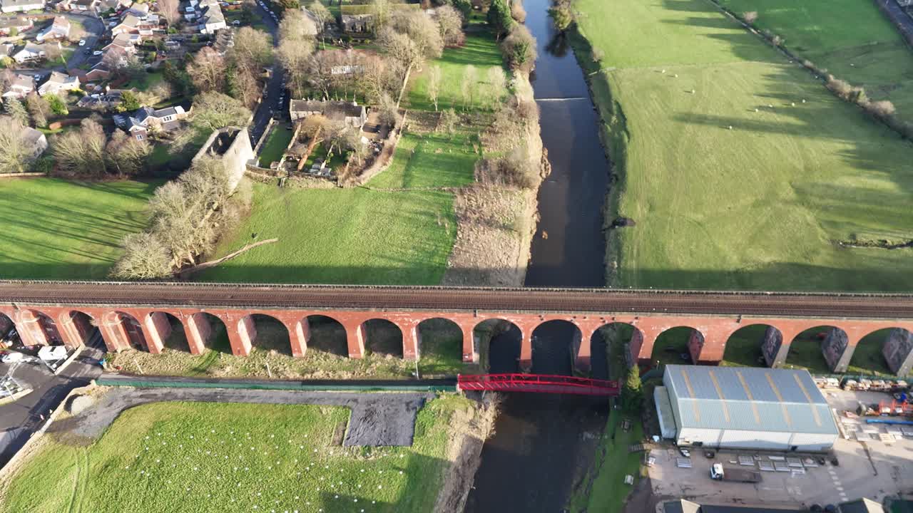 Aerial footage of a lush rural landscape in the UK, showcasing serene rivers, green pastures, and quaint villages under a clear blue sky, captured in golden hour light