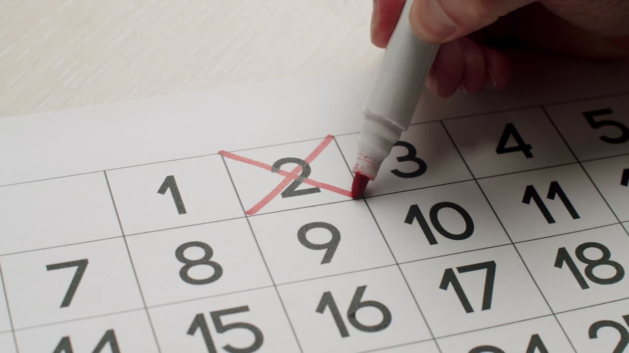 la mano del hombre escribe el segundo día en el calendario de papel usando un bolígrafo rojo.