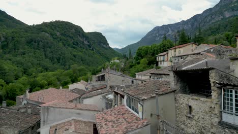 scenic drone shot of terracotta rooftops and cobblestone streets in a tranquil mountain village in france, framed by forested hills.