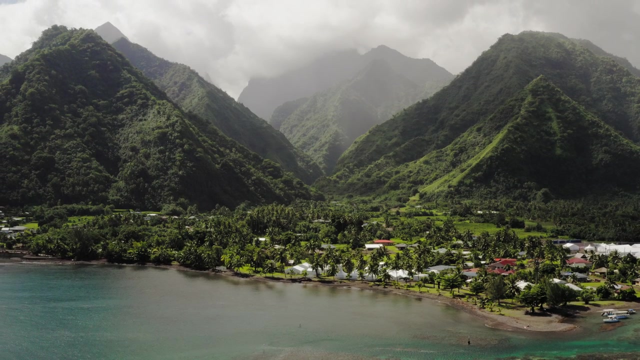 Teahupoo, Tahiti üzerindeki yağmur ormanı dağ sırası boyunca geniş panoramik drone geçişi, dağınık öğleden sonra bulutlarının altında katmanlanmış sivri sırtlar.