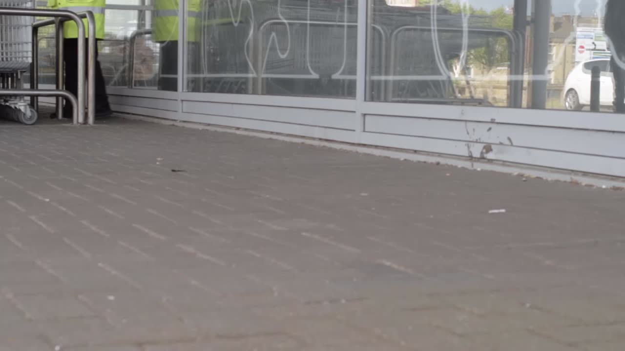 Supermarket trolleys outside a shopping centre with attendant walking by slow motion panning shot