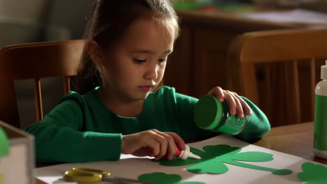 a young girl decorates shamrocks with glitter for st. patrick's day