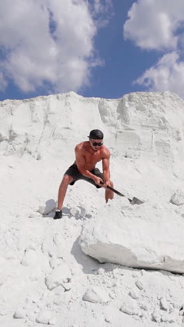 sportsman with huge hammer outdoors. sporty man demolishing big white rock by metal tool on the top of mountain in summer day. slow motion. vertical video
