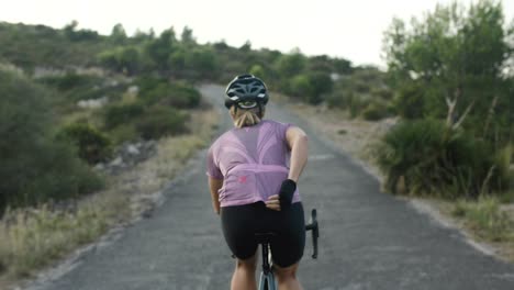 construir atleta femenina musculosa montando en bicicleta de carretera en un sinuoso camino de montaña en un hermoso día soleado de verano, vista desde la cintura hacia abajo, disparo medio